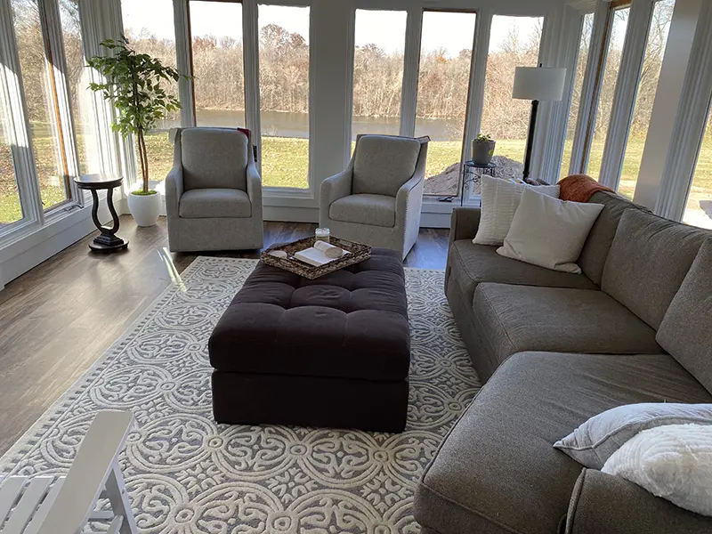 comfortable sectional and armchairs in a sunny sitting room with tall windows and an indoor plant interior design by Interiors of Distinction